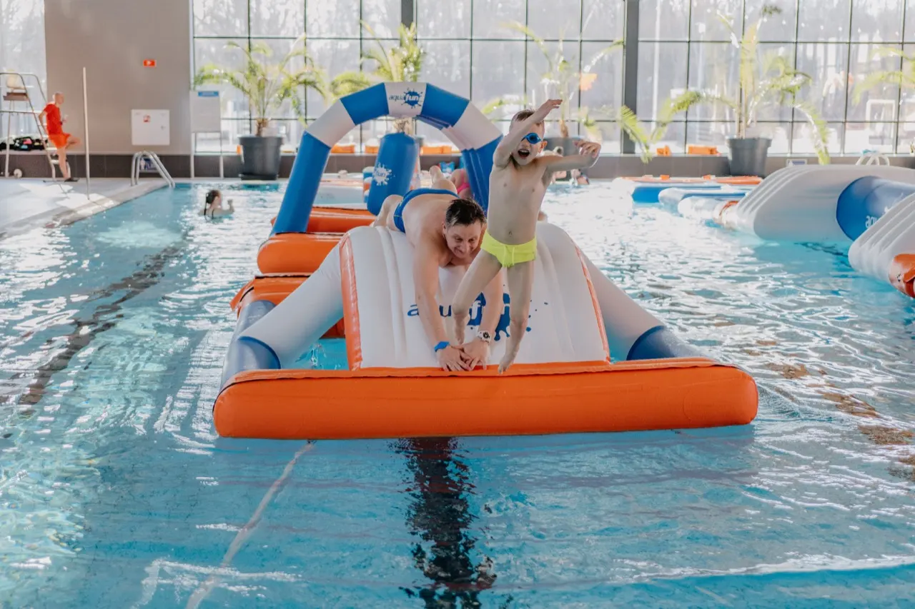 Dziecko skacze do wody ze zjeżdżalni kończącej tor przeszkód aquafun Pool Line na krytej pływalni